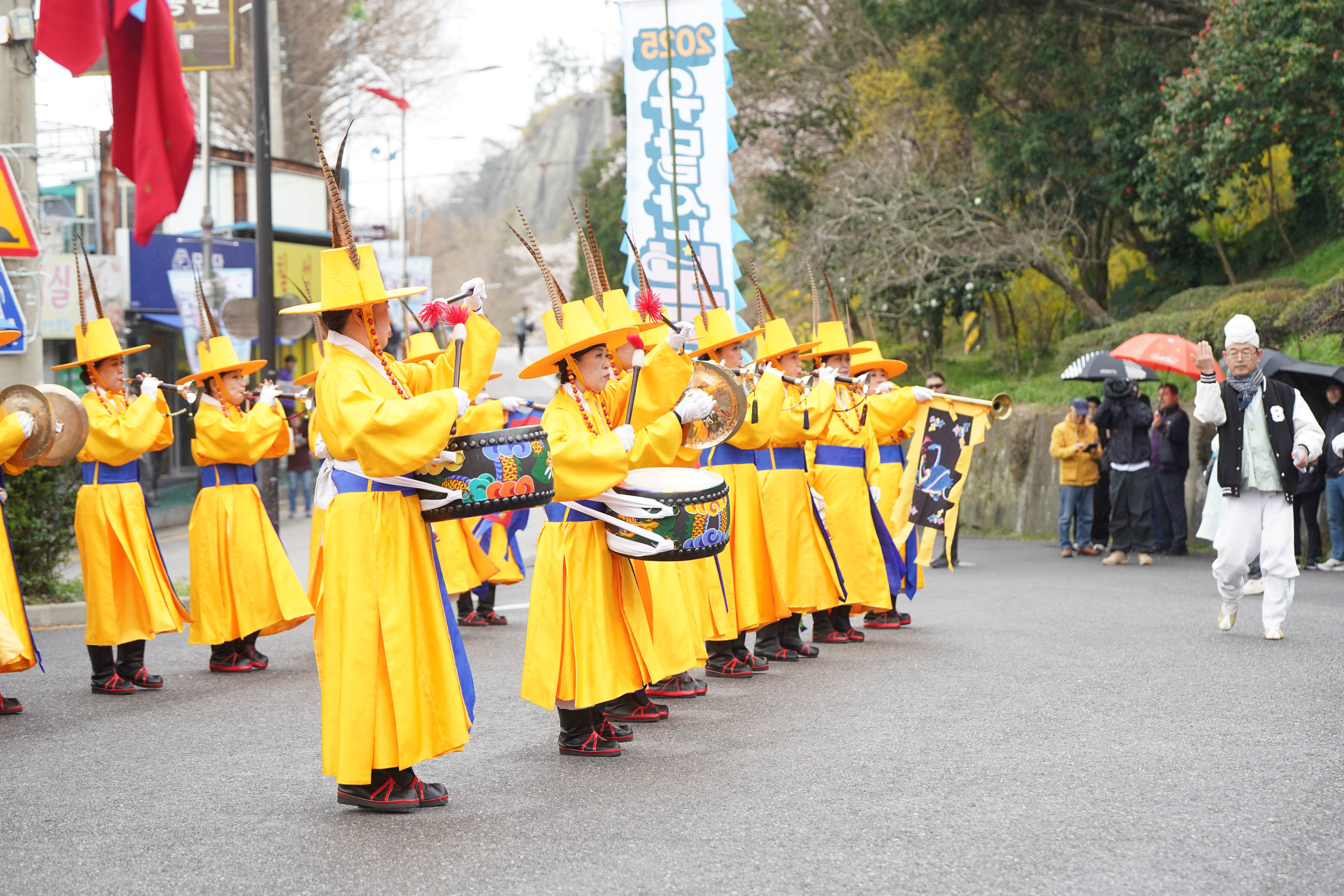 노란색의 전통복장을 입고 전통악기를 연주하는 행사관계자들과 그 모습을 구경하는 사람들