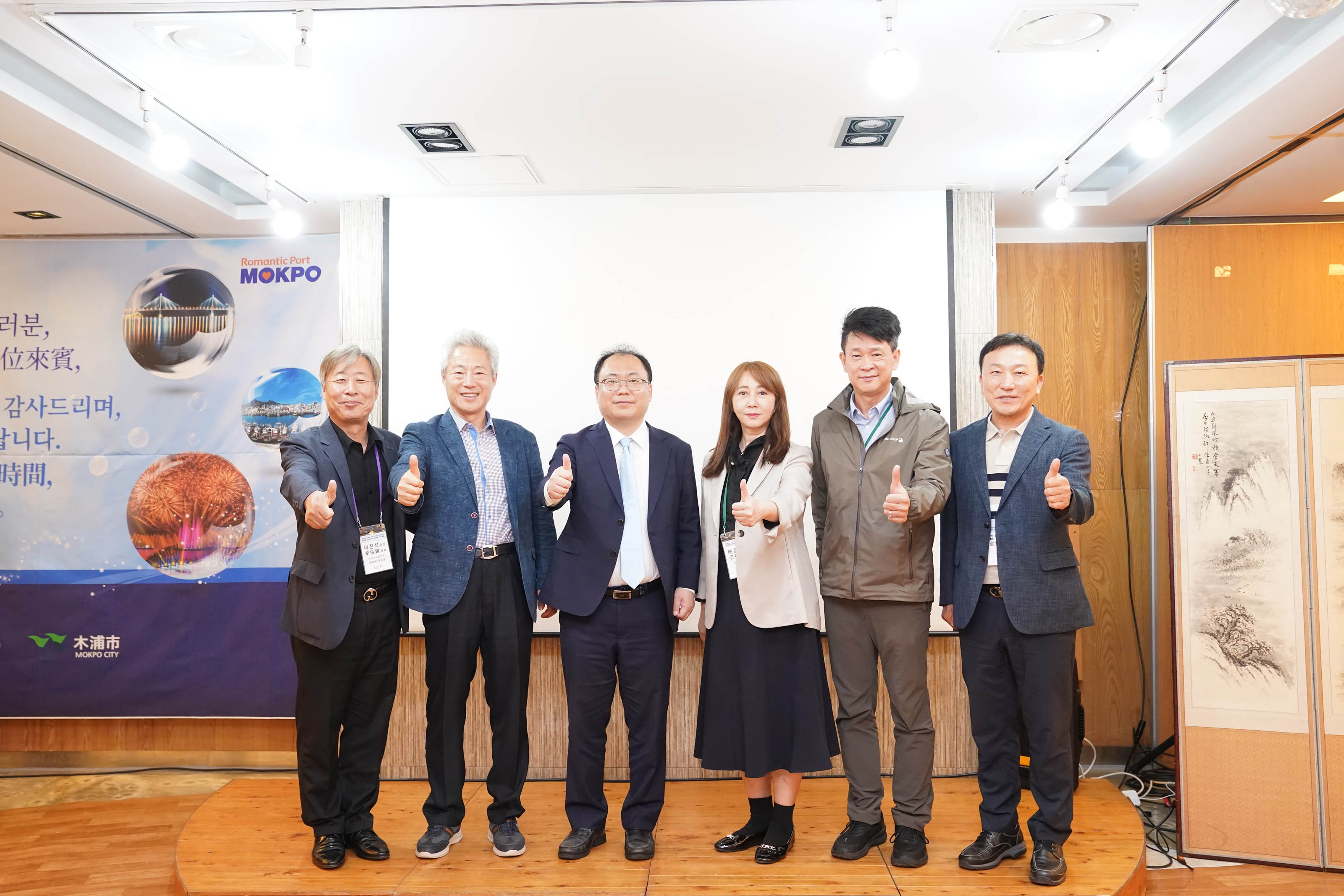 'Romantic Port MOKPO' 배경 앞에서 6명의 행사 관계자들이 나란히 서서 엄지손가락을 치켜세우며 기념 촬영을 하는 모습.