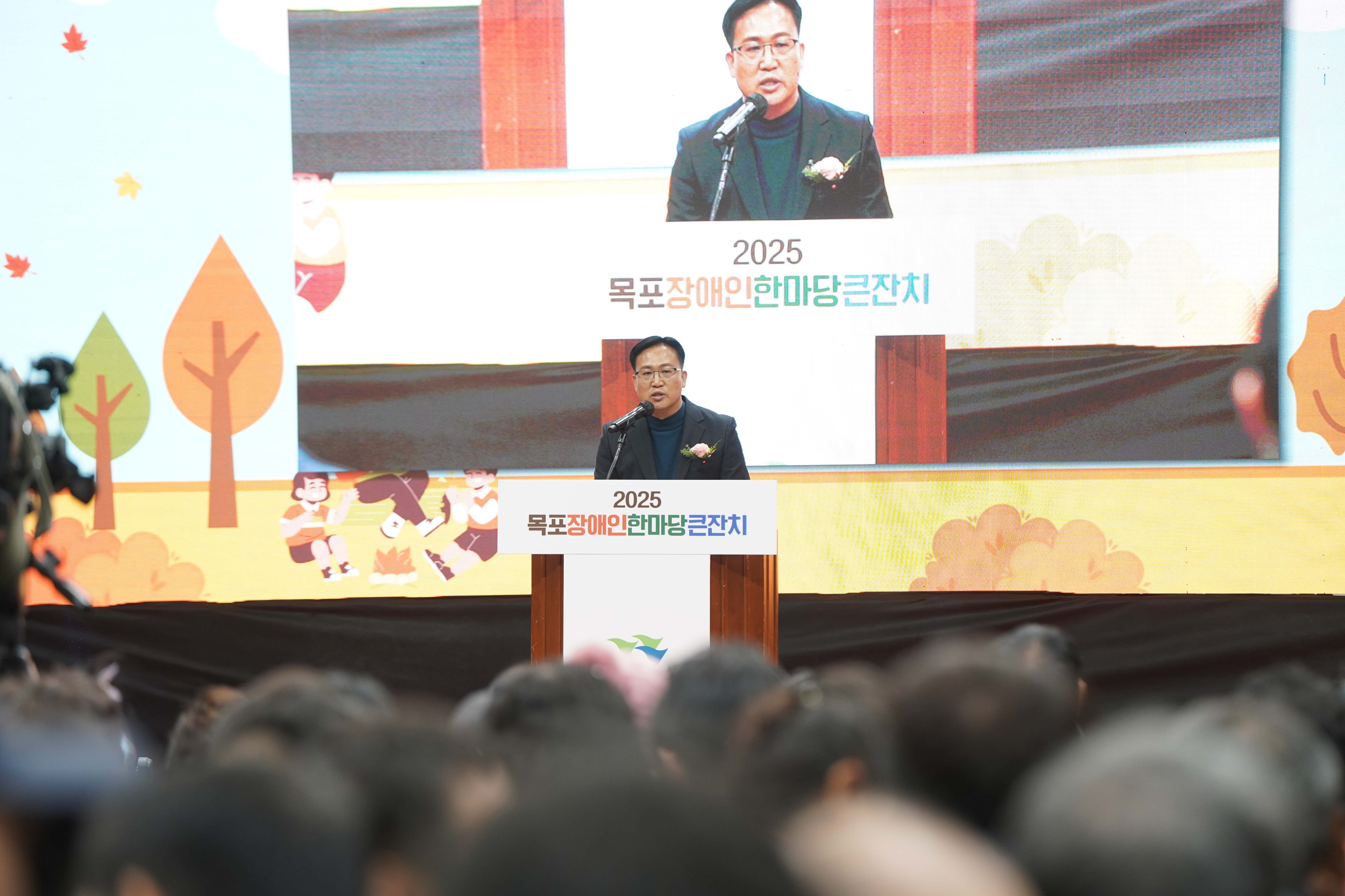 '2025 목포장애인 한마당큰잔치' 문구가 부착된 강단에서 조석훈 부시장이 축사를 하고 있는 모습. 배경 스크린에는 발언 중인 부시장의 모습이 크게 생중계되고 있음.