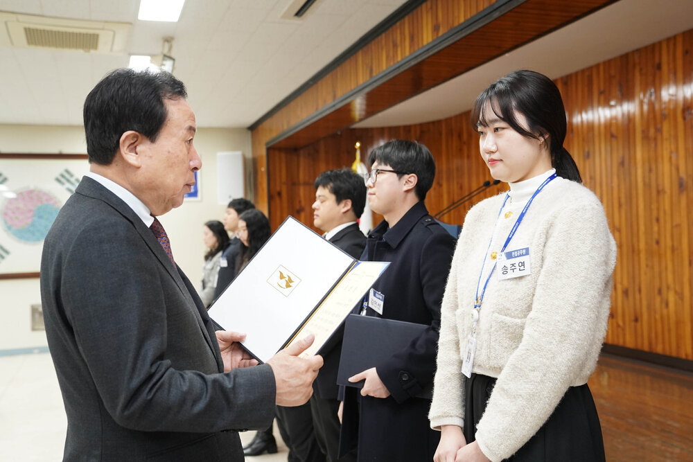 3월 정례조회에서 정장을 입은 남성이 아이보리 니트를 입은 여성에게 표창장을 전달하는 모습