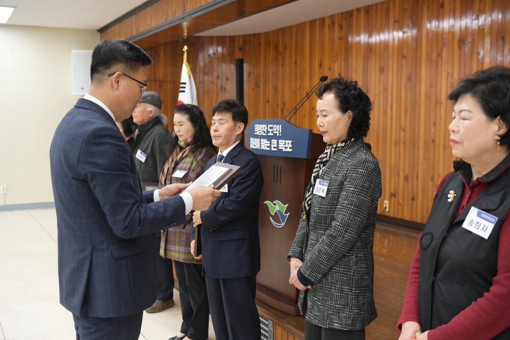 3월 정례조회에 정장을 입고 안경을 낀 남성이 짧은 파마머리에 회색과 흰색이 트위드자켓을 입은 김은숙에게 패를 수여하고 있다.