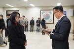 2026년 상반기 4급이하 정기인사로 정장을 입고 안경을 쓴 남성이 실내 행사장에서 한 여성에게 상장을 전달하며 내용을 읽고 있고, 여성은 검은 코트와 안경을 착용한 채 두 손을 모은 채 서 있으며 뒤쪽에는 참석자들이 줄지어 서서 행사를 지켜보고 있다.
